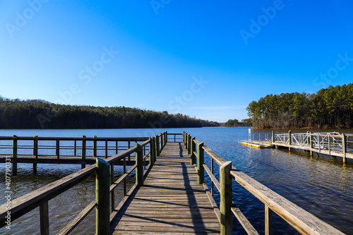 a majestic shot of the still blue lake waters of Lake McIntosh in Peachtree City, Georgia with lush green and autumn colored trees and grass with blue skies photo