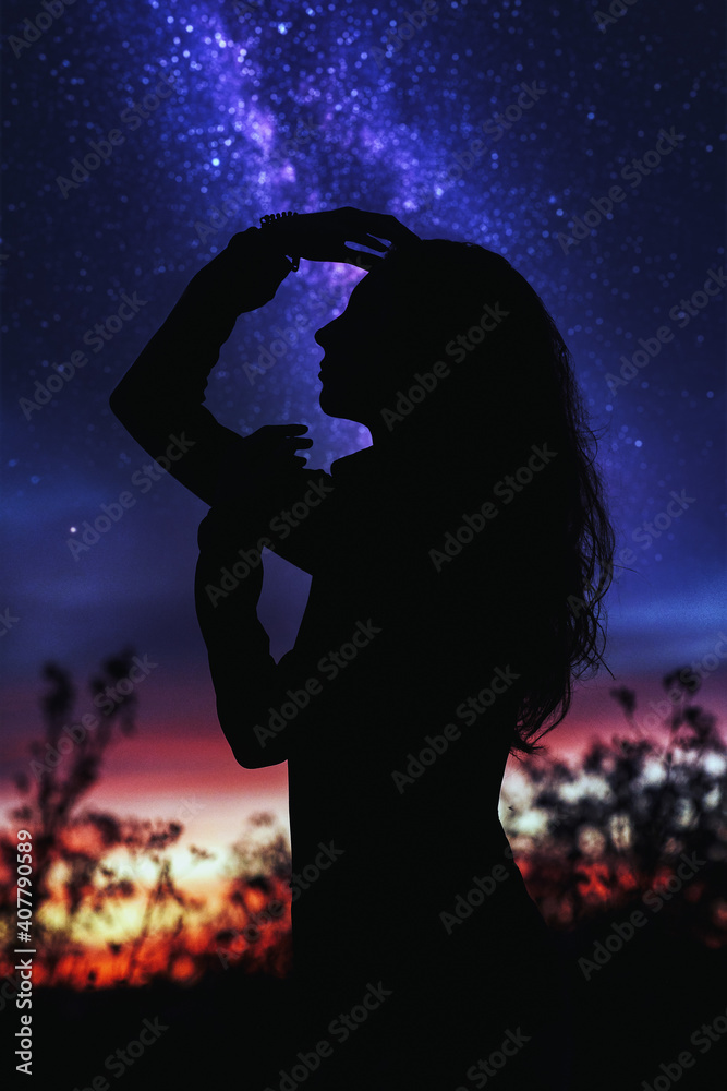 Woman posing nicely, observing the universe against the backdrop of the shining Milky Way galaxy and a beautiful sunset. Silhouette of a woman against the background of blurry stars