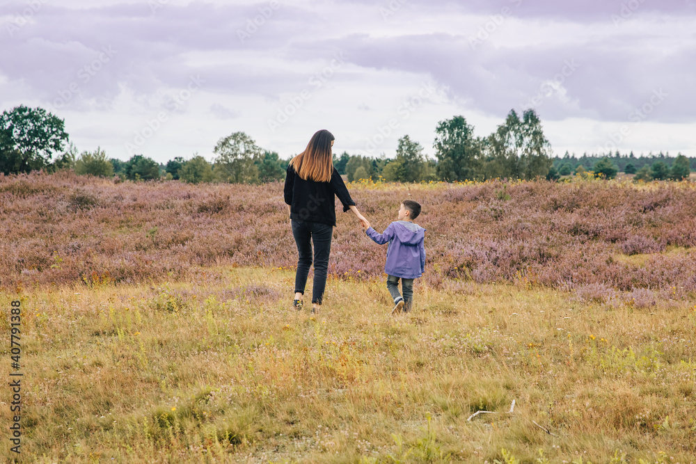 woman walking in the field. Brunette woman in black jeans walks through a blooming heather meadow with a child by the hand. Mother and child in nature. Lüneburg Heath in Germany woman walking in the field. Brunette woman in black jeans walks through a blooming heather meadow with a child by the hand. Mother and child in nature. Lüneburg Heath in Germany