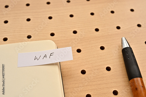 A sticky note with WAF written on the edge of an open notebook on the punching board. That's an acronym for Web Application Firewall. photo