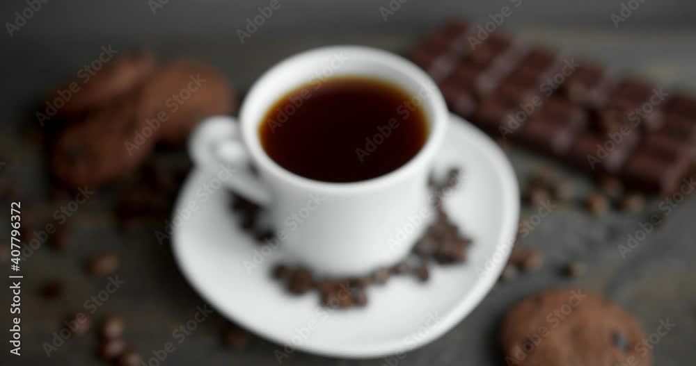 Cup of coffee with cookies, chocolate and roasted coffee beans scattered on a wooden table. Black coffee mug. Fresh arabica roasted coffee beans. Great start of morning. Espresso, americano, doppio. Cup of coffee with cookies, chocolate and roasted coffee beans scattered on a wooden table. Black coffee mug. Fresh arabica roasted coffee beans. Great start of morning. Espresso, americano, doppio.