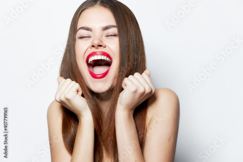 Woman with bare shoulders laughs with his mouth wide open and hands near his face lipstick 