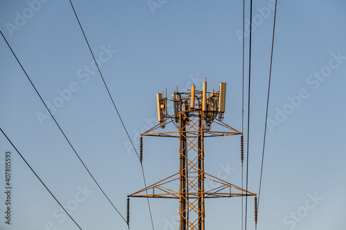 Mobility telecom panel antennas on the top of a power line lattice tower, in late afternoon light
