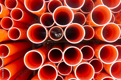 Stacked bright orange electrical conduit pipes end on making a pattern of circles.