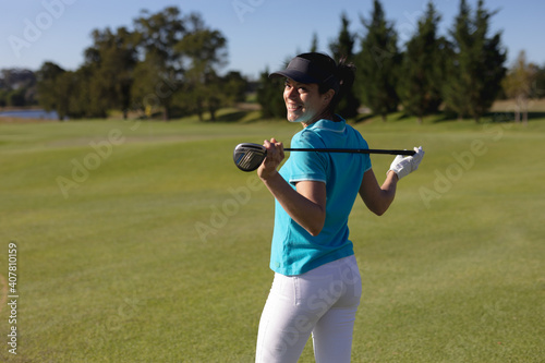 Caucasian woman on golf course holding golf club across shoulders smiling to camera
