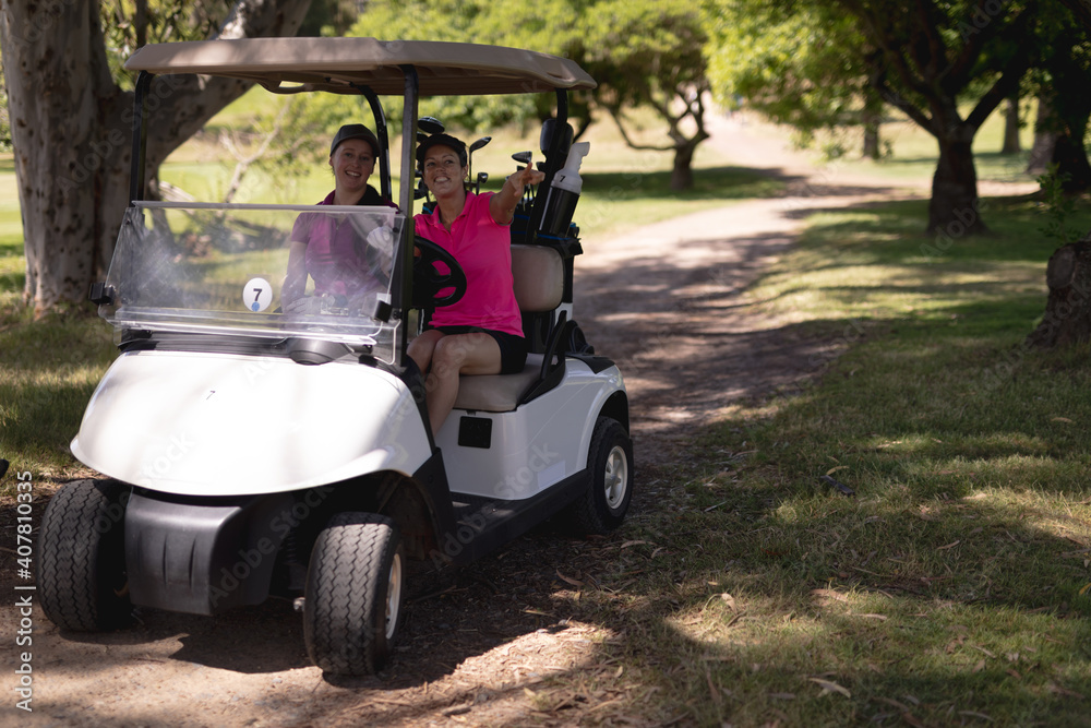 Two caucasian woman driving a golf cart with clubs on the back at golf course Two caucasian woman driving a golf cart with clubs on the back at golf course