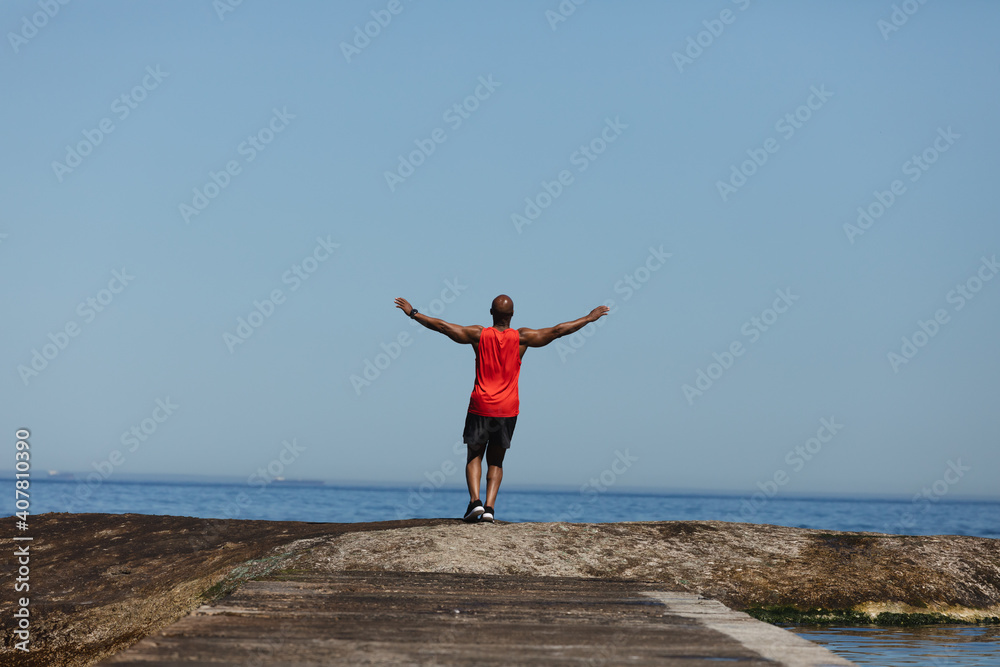 Rear view of fit senior african american man exercising by sea with arms outstretched Rear view of fit senior african american man exercising by sea with arms outstretched