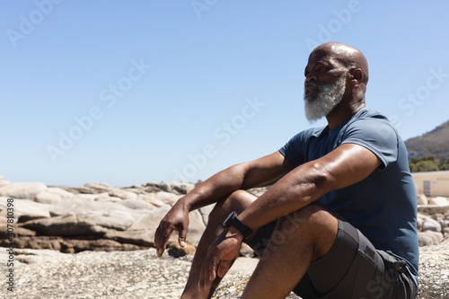 Fit senior african american man sitting on rocky coast looking away