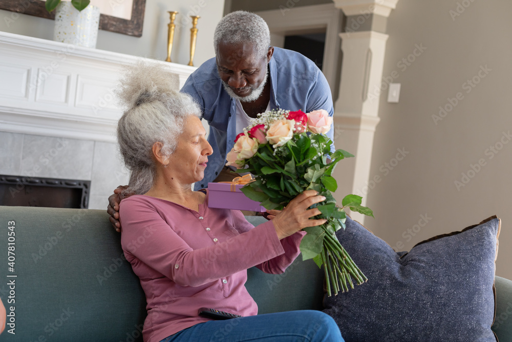 Senior mixed race couple in living room man giving woman flowers