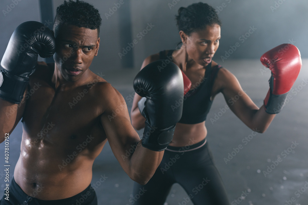 African american man and woman wearing boxing gloves throwing punches in air in empty building African american man and woman wearing boxing gloves throwing punches in air in empty building
