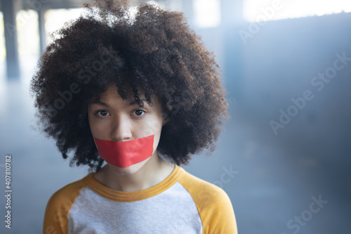 Mixed race woman with tape on mouth looking at camera photo