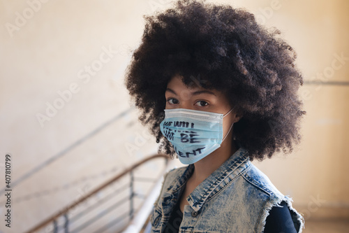 Mixed race woman wearing face mask with slogan looking at camera photo