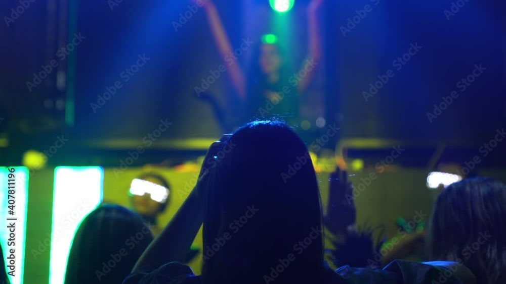 Group of people dance in disco night club to the beat of music from DJ on stage . New year night party and nightlife concept .