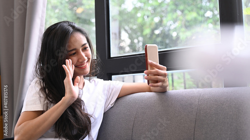 Young woman using smart phone video call with her friends while sitting on sofa at home.