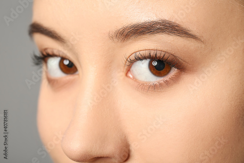 Young woman with beautiful eyebrows on grey background, closeup