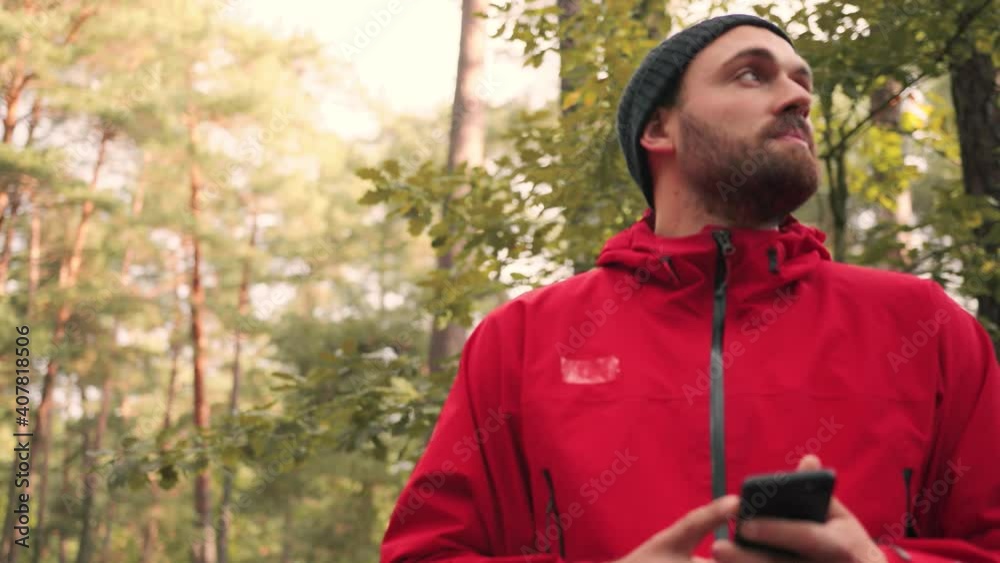 Happy traveling man in hat travels through the woods, looking at nature around smiling and holding smartphone. Happy traveling man in hat travels through the woods, looking at nature around smiling and holding smartphone.
