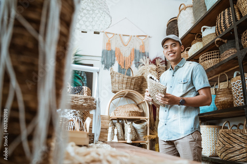 young entrepreneur smiles while holding a wicker wallet while standing in a craft shop