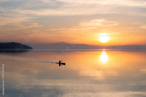 Beautiful sunset at Trasimeno lake with a man on a canoe above perfectly still water