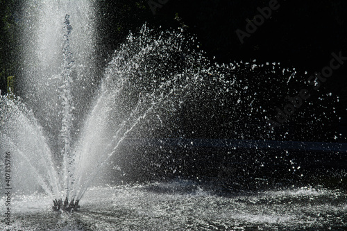 Close-up on the water jet of a round fountain in a park in Brussels. It falls back in large drops, lit by a summer sun. Dark background. Summer in the capital, Belgium