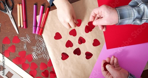 Close-up of children and elderly hands making handmade cards by laying out hearts on paper. Love, family and Valentine's day concept