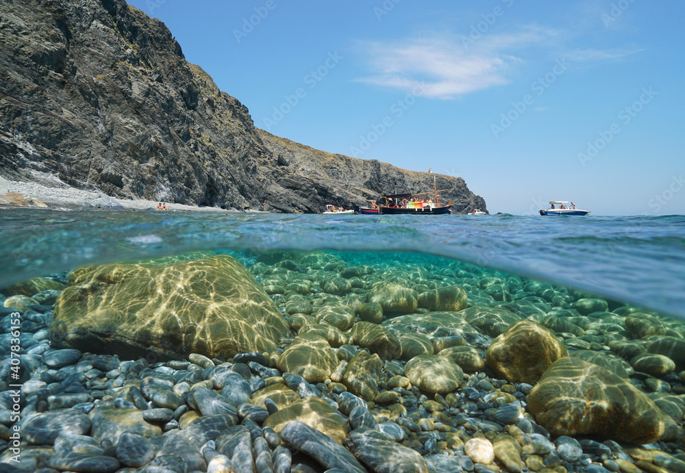 Seascape Mediterranean sea, rocky coast with boats and pebbles with rocks underwater, split view half over and under water, Cap Cerbere at the border between Spain and France