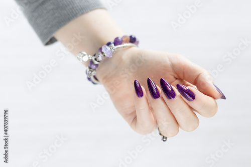 Photo Female hand with long nails and a bottle with purple nail polish
