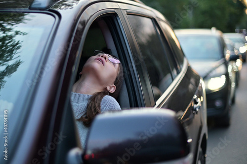 Young woman stands in a traffic jam and looks out through the window