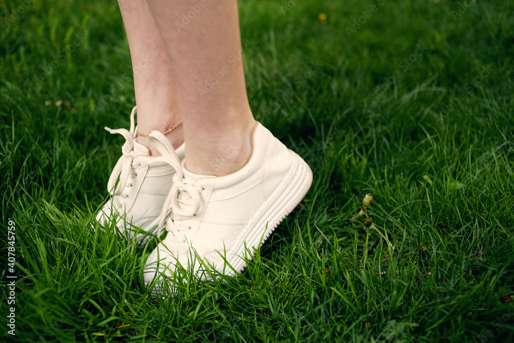 Woman in white sneakers in the park walk green grass