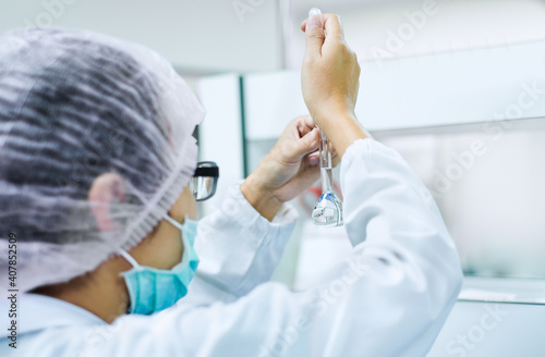 The chemist working in the chemical laboratory she is looking and adjust the volume of solution in the amber volumetric flask, pharmaceutical concept photo