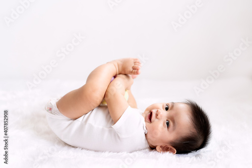 A cute 6 months old asian little baby boy is playing his hands and feet with fully happiness moment on the bed in the morning time, concept of healthy and child development in the first year of life.