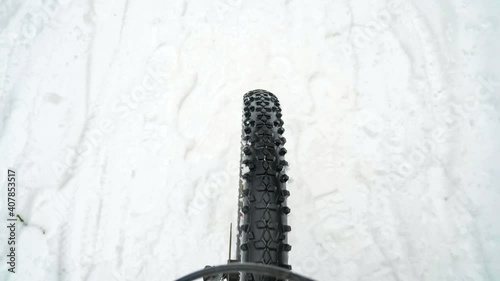 Fatbike front wheel riding on slippery snowy road. Slow motion of cycling in winter. Rotating tire with high plugs on a tread pattern. Extreme sports. photo