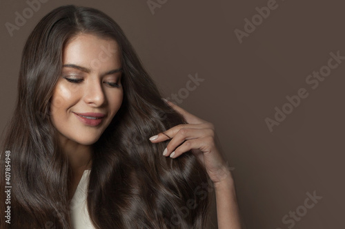 Lovely brunette woman with long healthy hair on brown background, fashion beauty portrait
