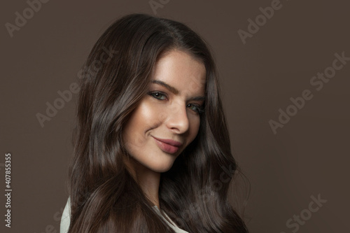 Beautiful young woman face with healthy clear skin and long hair on brown background