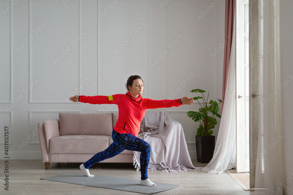 Middle aged woman practices yoga at home. Archer Pose. Middle aged woman practices yoga at home. Archer Pose.