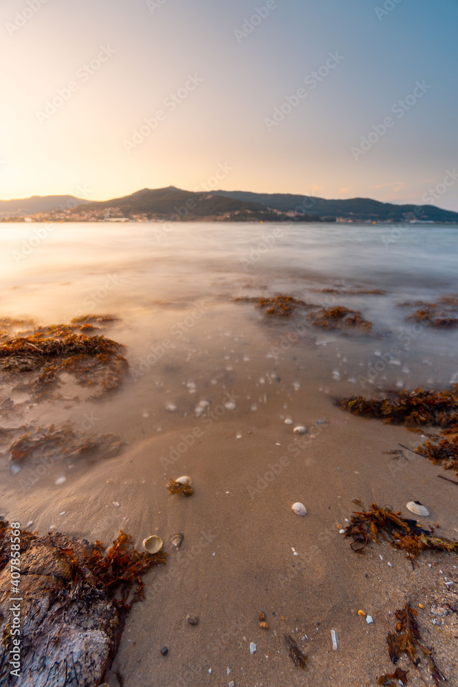 Beautiful beach with sunset light and coastline in the background. With the sea blurred and transparent. Sand and shells