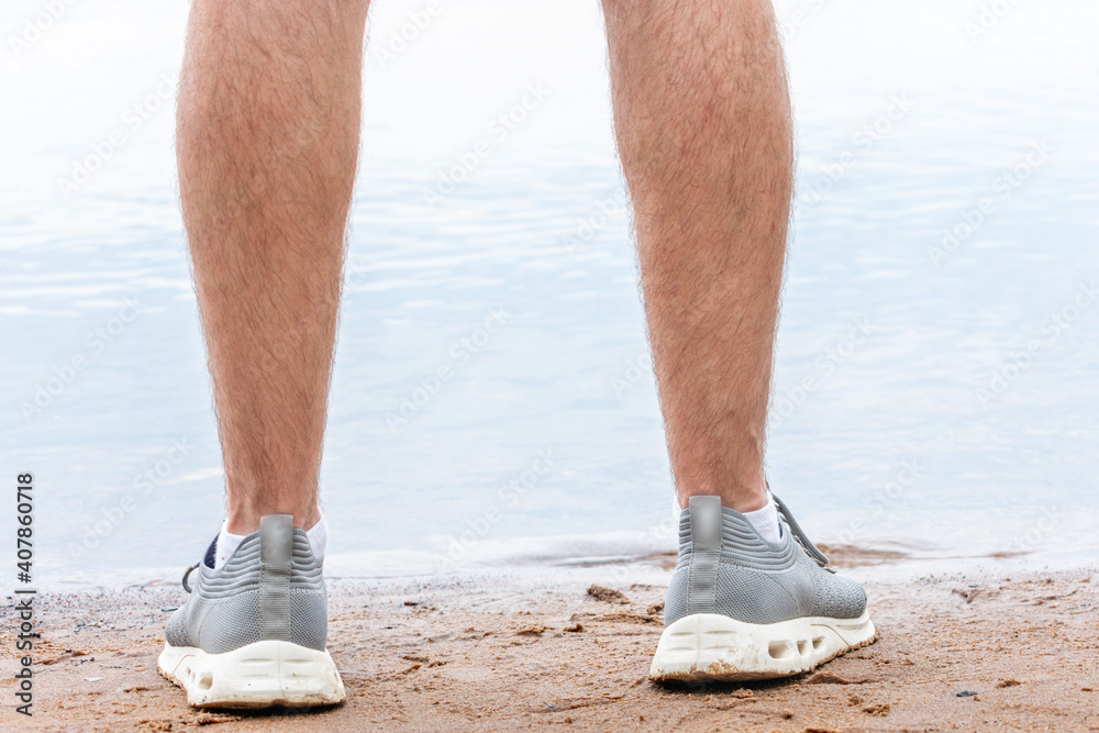 Man in sneakers stands on the shore of the lake, men's feet, close up, cropped image