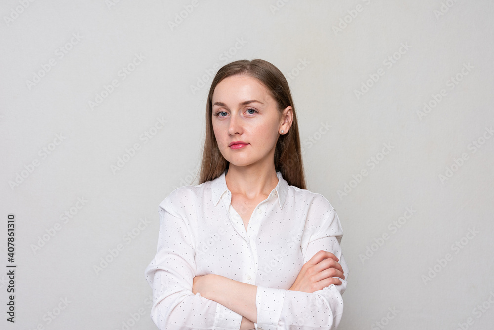 Young serious woman with her arms crossed looks at the camera, white background Young serious woman with her arms crossed looks at the camera, white background