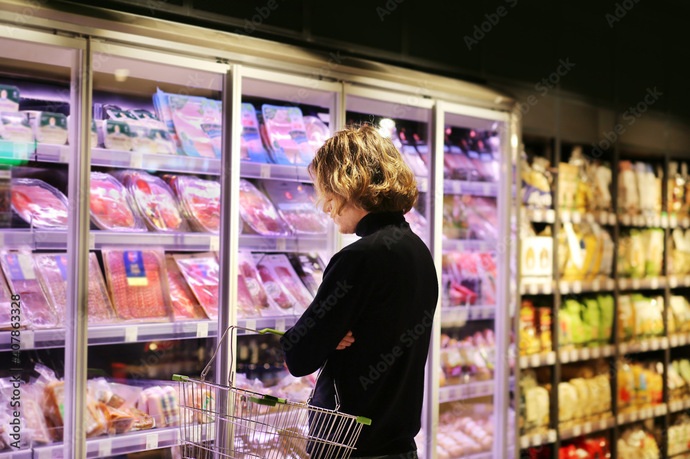 young man shopping in supermarket, reading product information.