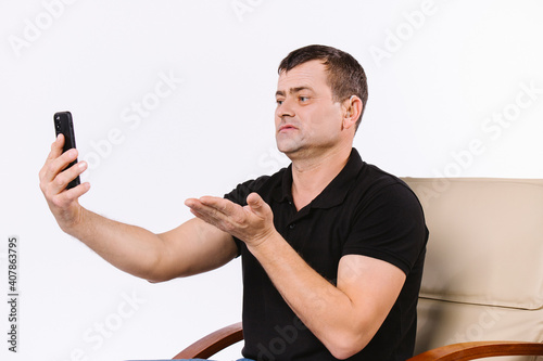 Caucasian surdomute man communicates non-verbal via video call by stretching out his thick palm towards the camera while sitting in a chair. White background. photo