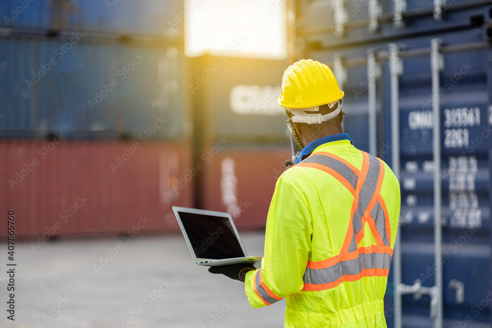 worker man in protective safety jumpsuit uniform with yellow hardhat and use laptop check container at cargo shipping warehouse. transportation import,export logistic industrial service worker man in protective safety jumpsuit uniform with yellow hardhat and use laptop check container at cargo shipping warehouse. transportation import,export logistic industrial service