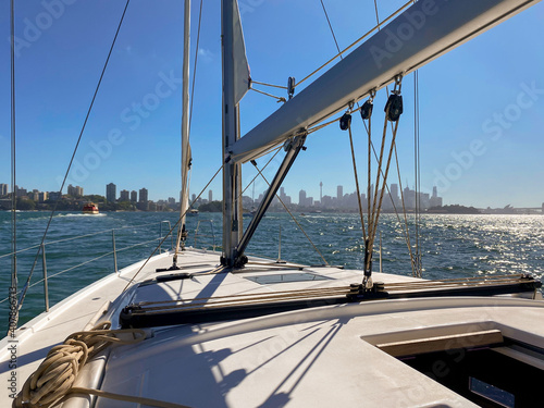 Yacht sailing towards the city in Sydney Harbor  on a sunny day. View from the boat s cockpit over into city skyline