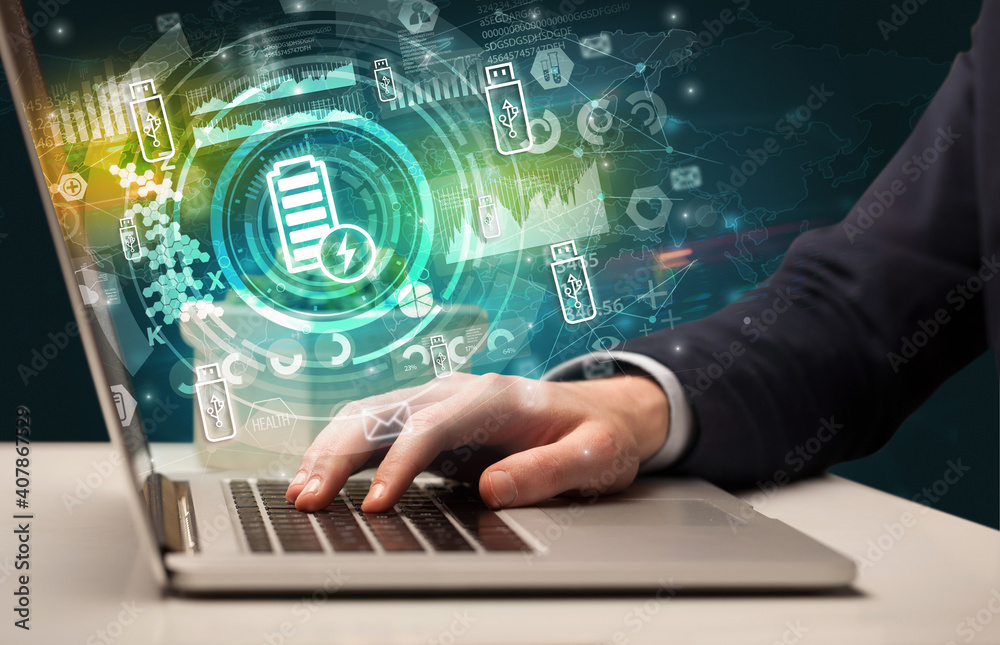 Business hand typing on a modern laptop with battery charging icon coming out from multimedia screen, intuitive technology concept Business hand typing on a modern laptop with battery charging icon coming out from multimedia screen, intuitive technology concept