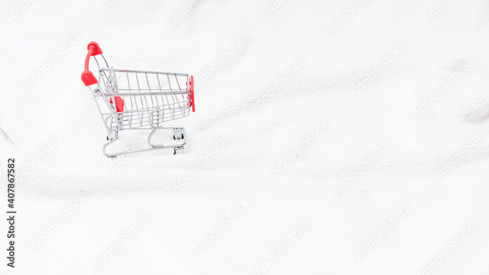 Shopping cart on a white snow, crumpled blanket, top view, copy space, 16:9