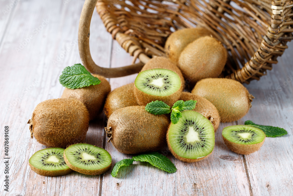 Ripe raw kiwi green whole and slices falling from basket with  mint leaves