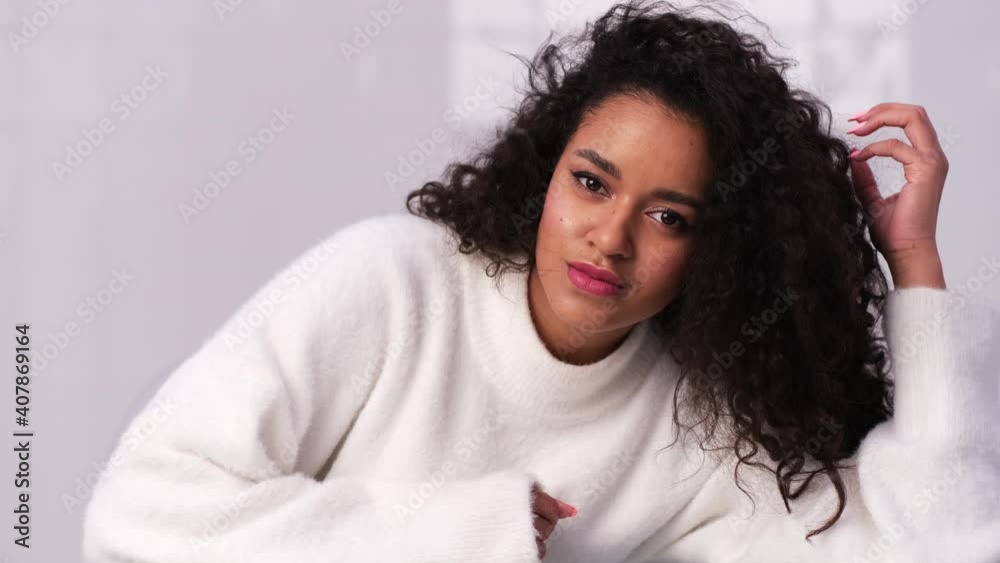 Camera zoom on face of young biracial girl with afro hairstyle and modern makeup posing flirting. Natural beauty concept