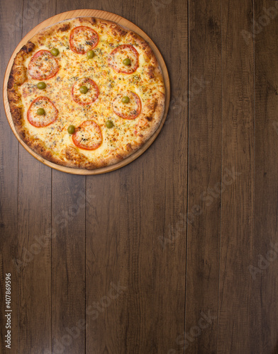 Tasty mozzarella cheese pizza with slices of red tomatoes on a wooden board. Vertical top shot with food aligned on the upper left side. Space for texts.