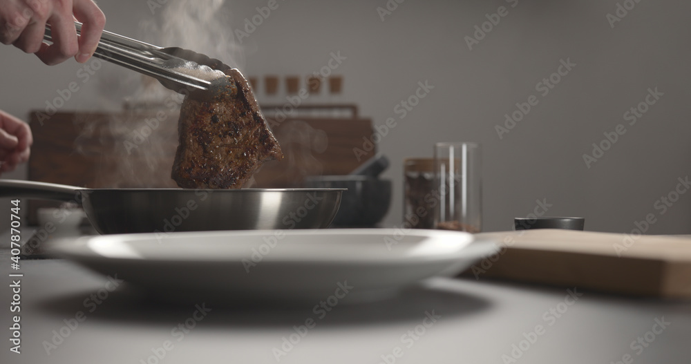 Fototapeta premium man put whole beef steak on black plate on concrete countertop