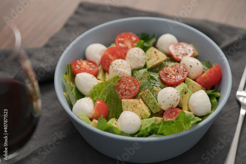Salad with romaine, tomatoes and mozzarella in blue bowl with glass of red wine