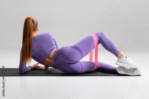 Fitness woman doing clamshell exercise for glutes with resistance band on gray background Fototapet