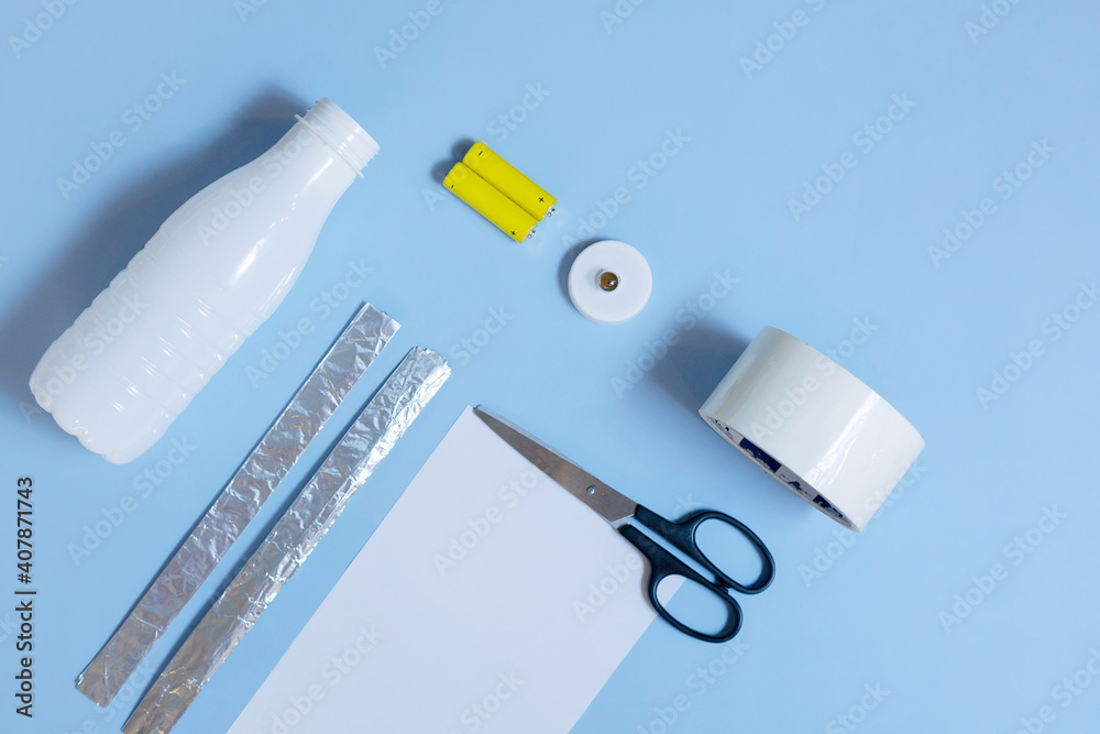 Flat lay of an empty plastic bottle, foil, batteries, lid, light bulb, scissors are on a blue background. The concept of upcycling, the making of a flashlight, the second step. Flat lay of an empty plastic bottle, foil, batteries, lid, light bulb, scissors are on a blue background. The concept of upcycling, the making of a flashlight, the second step.
